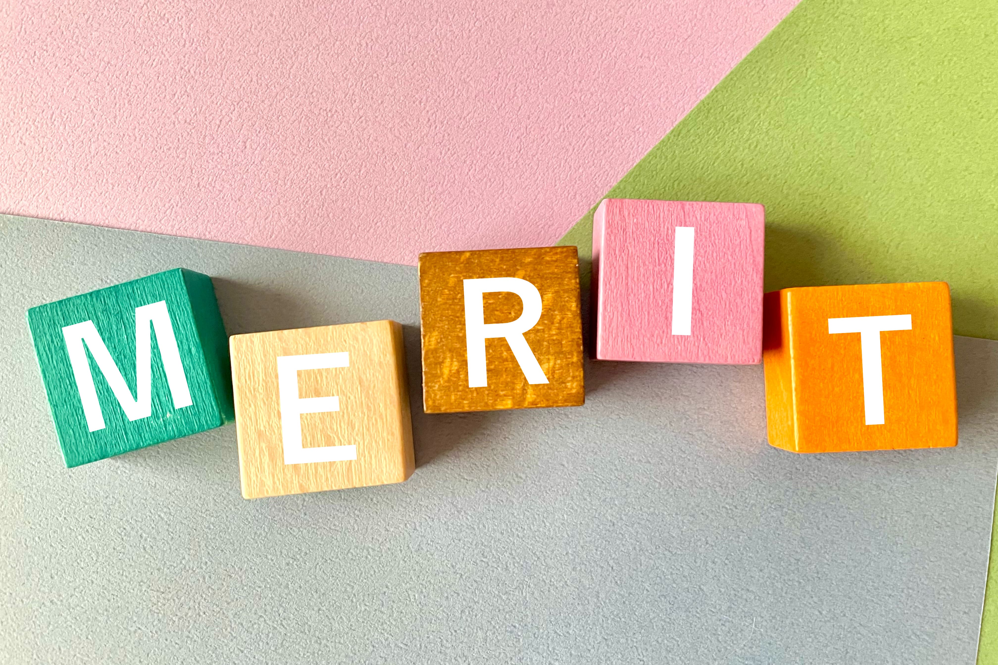 カラフルな背景に並べられた木製ブロックで『MERIT』と書かれた文字