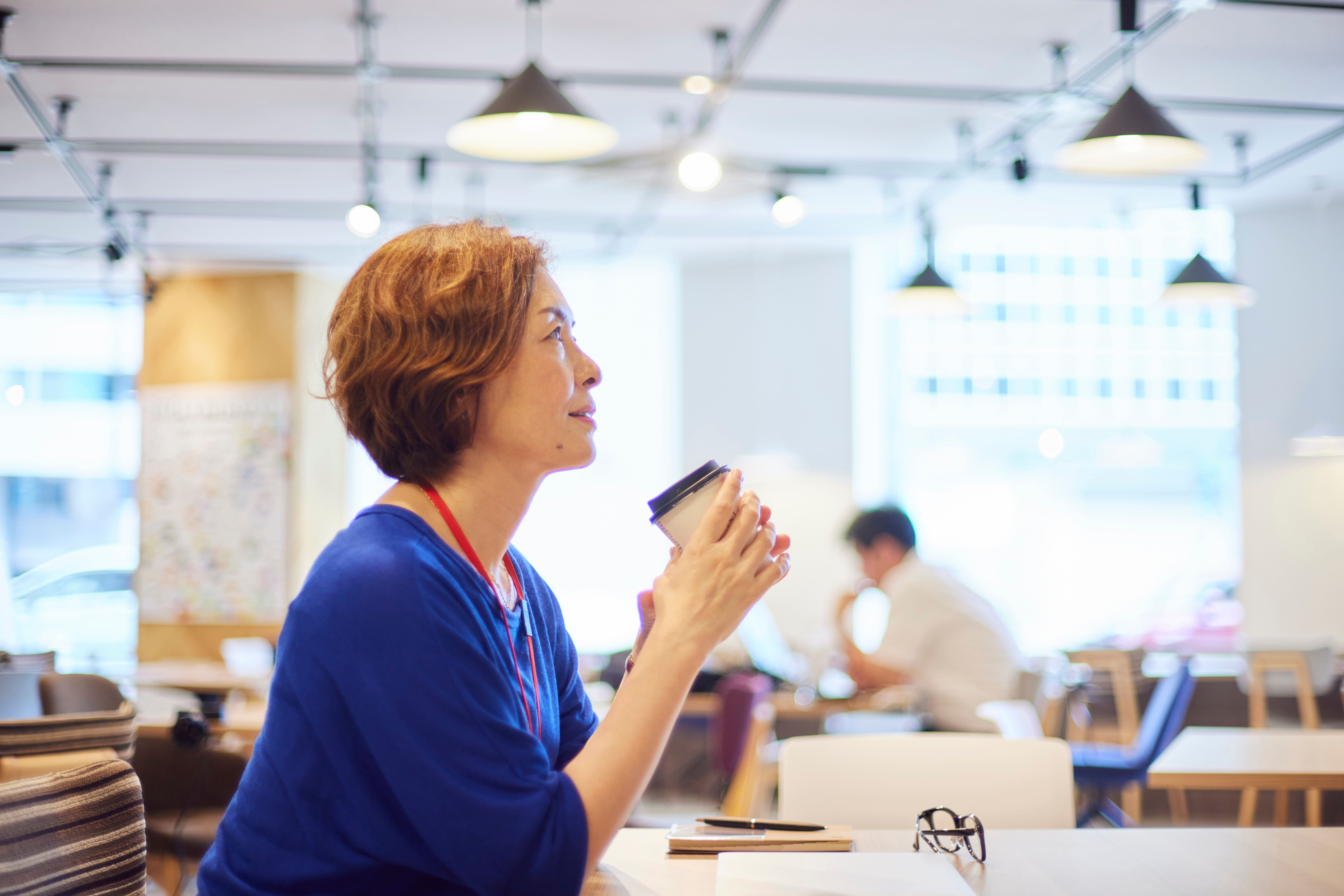 オフィスのカフェスペースで紙カップのコーヒーを持ちながらくつろぐビジネスパーソン
