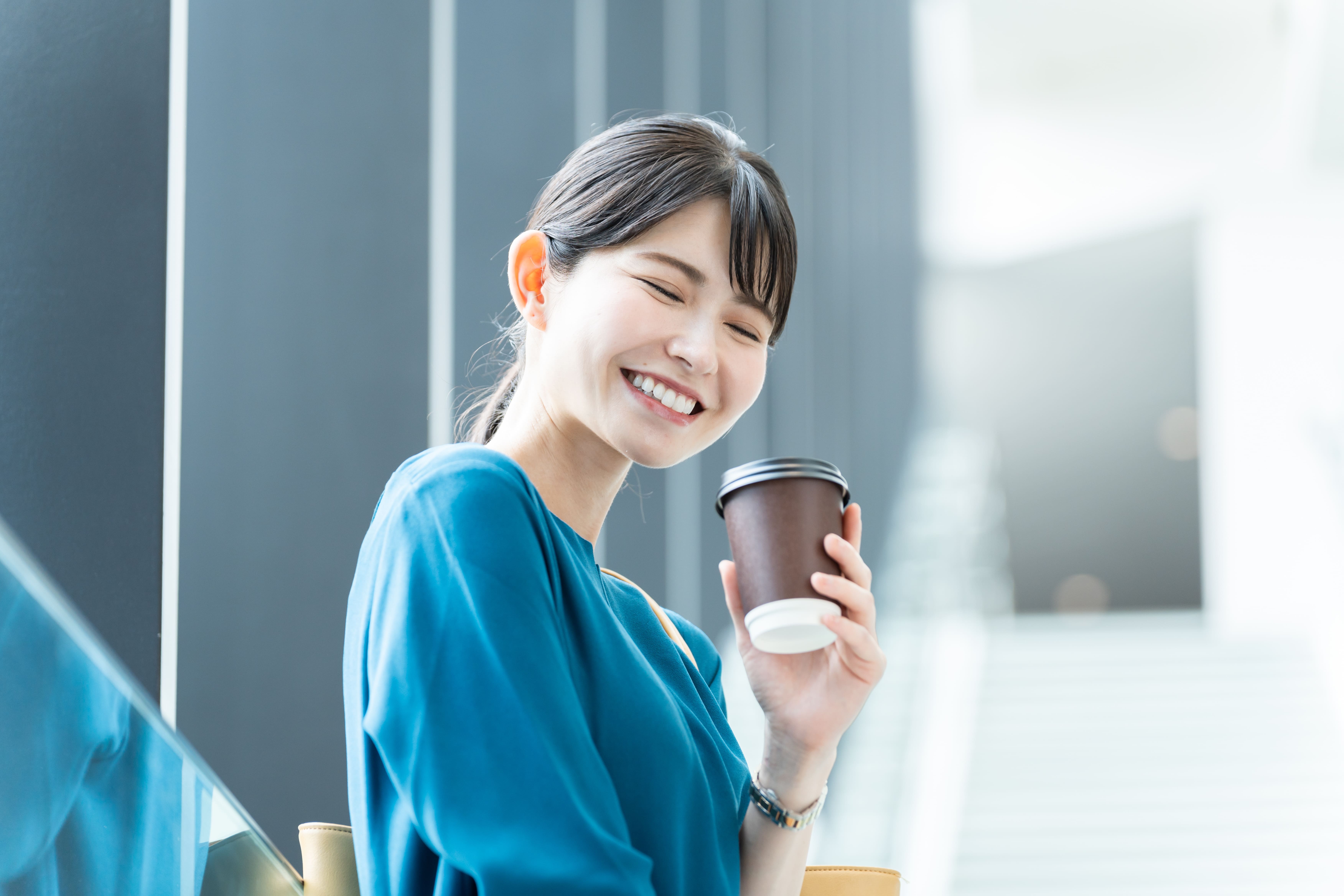 オフィスのカフェスペースで紙カップのコーヒーを持ちながら過ごすビジネスパーソン