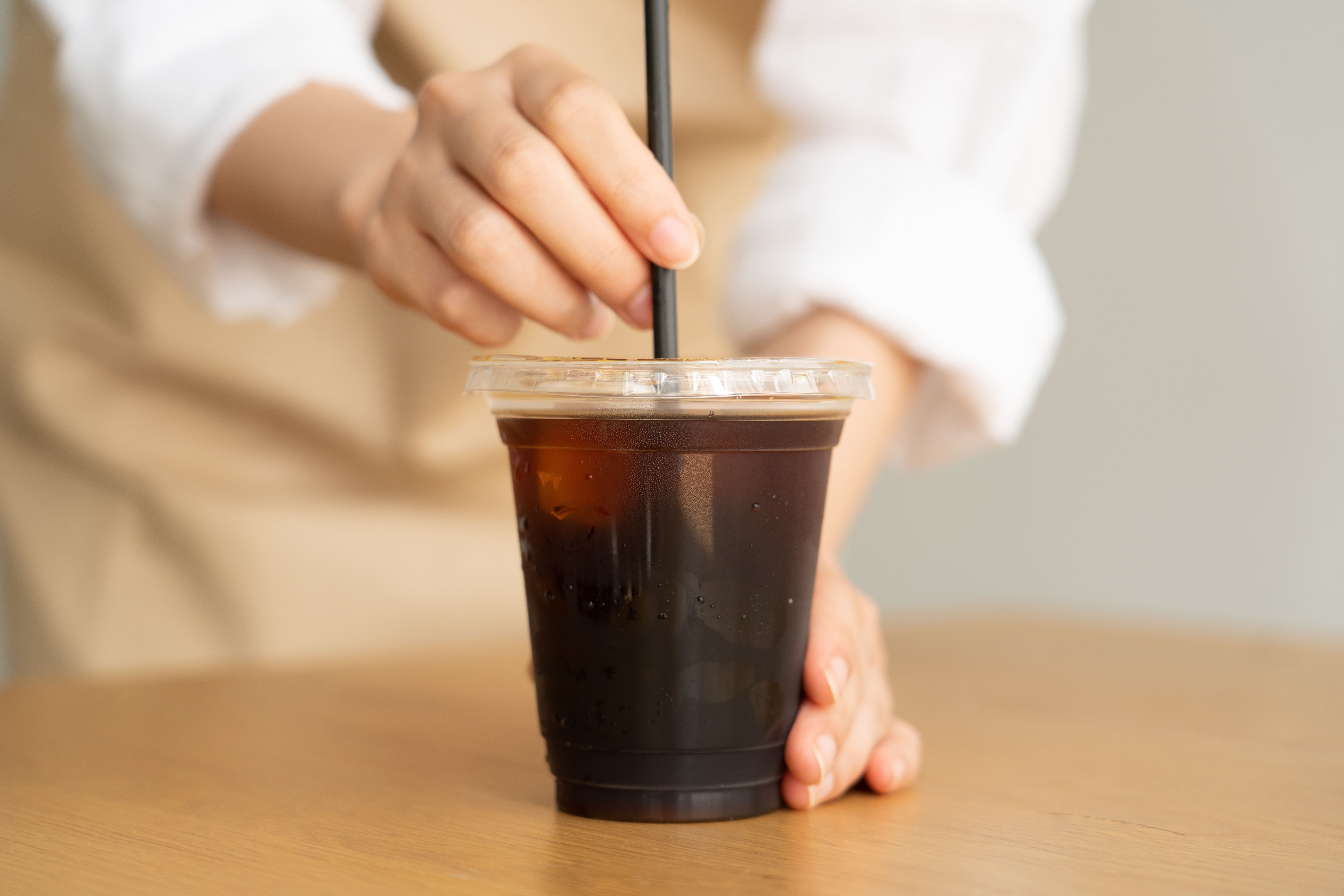 プラスチックカップに入ったアイスコーヒーをストローでかき混ぜる様子