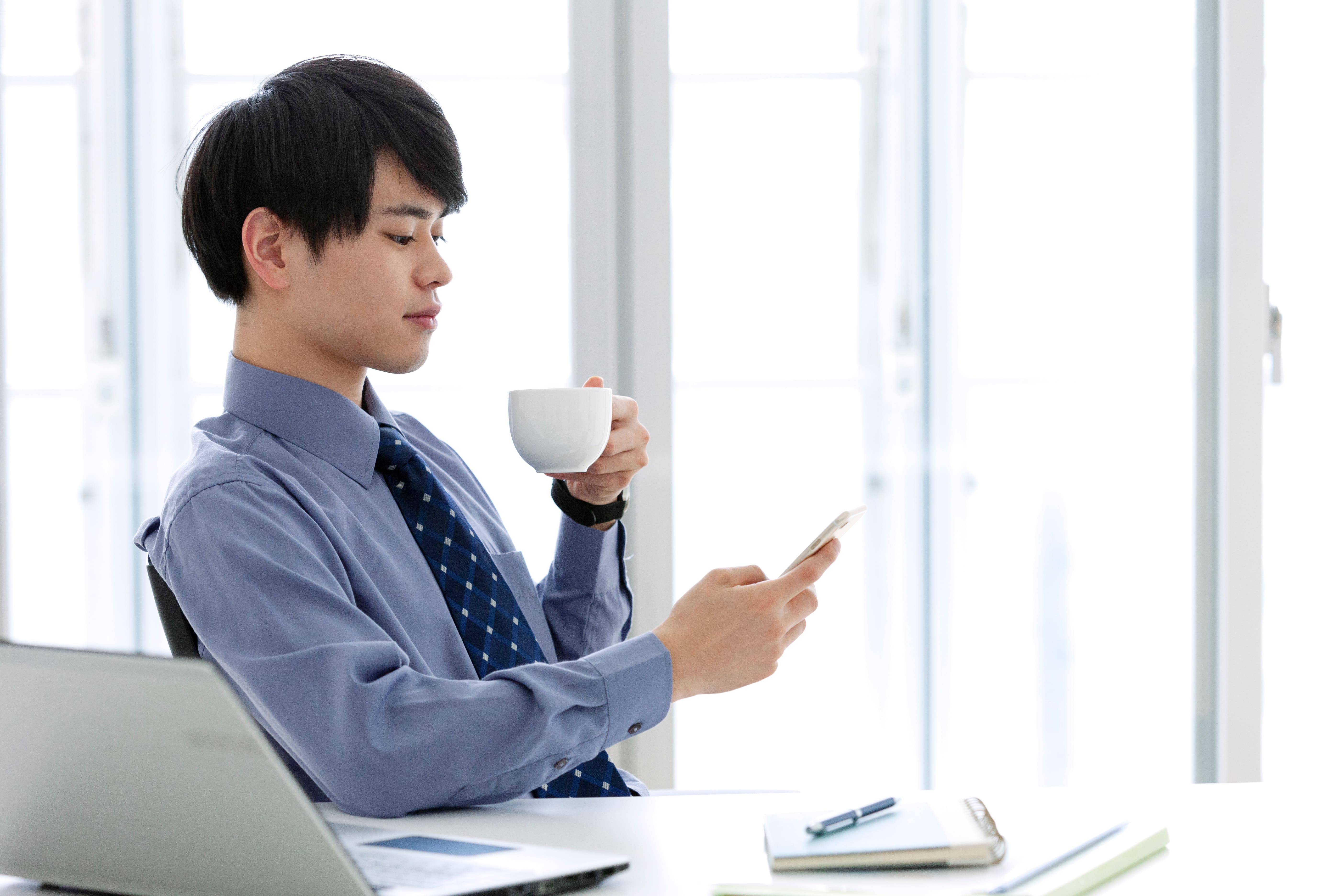 オフィスコーヒーを楽しみながらスマートフォンで情報を確認する様子