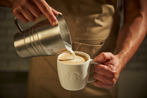 エプロンを着たバリスタがスターバックスのコーヒー体験をお届けするカフェラテを作っている様子