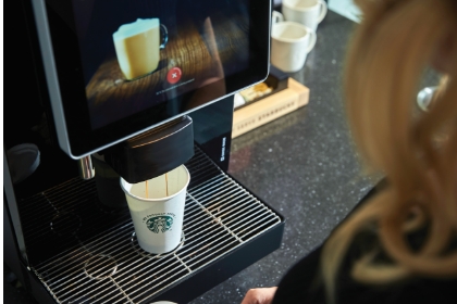 FRANKEコーヒーマシンでWe Proudly Serve Starbucks®のカップにカフェラテを注いでいる様子